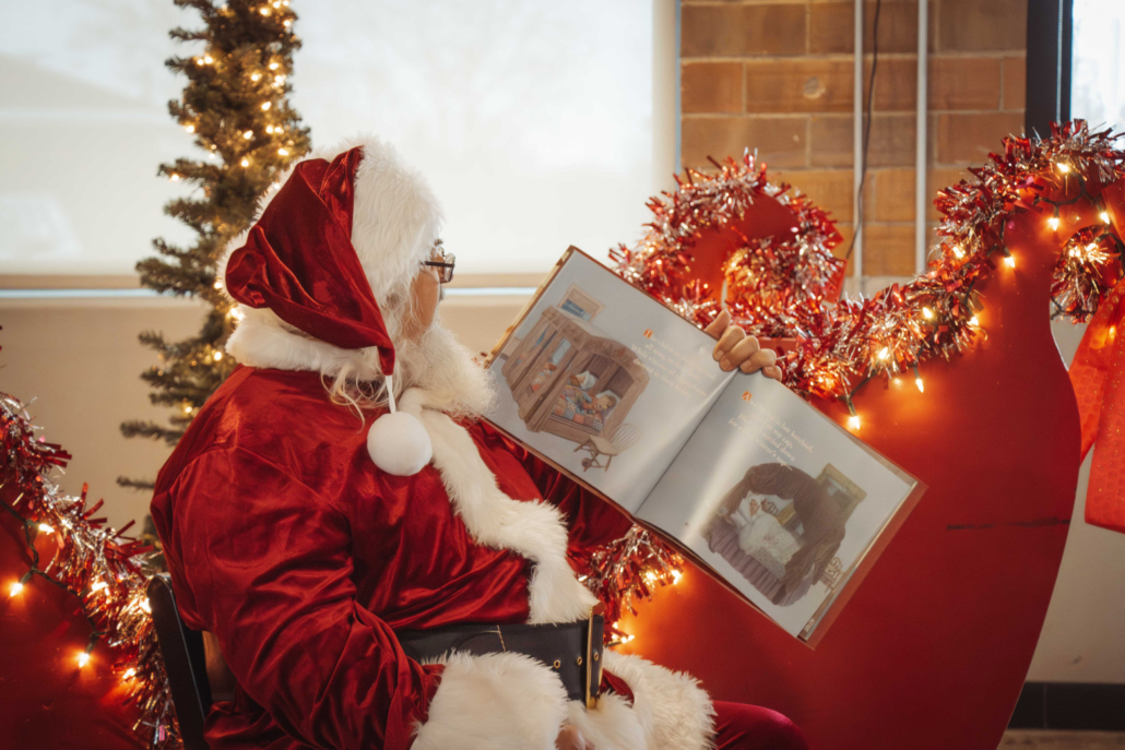Santa Claus reading in front of a red sleigh at Terra Square.