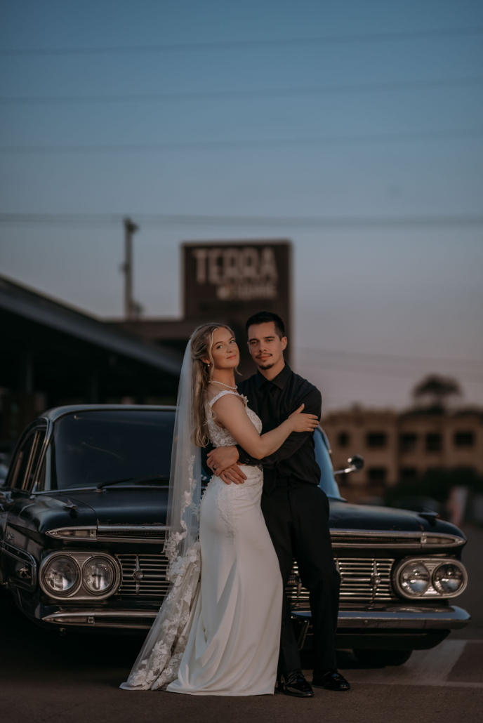 Bride and groom pose in front of a vintage car parked in front of Terra Square in Hudsonville, Michigan
