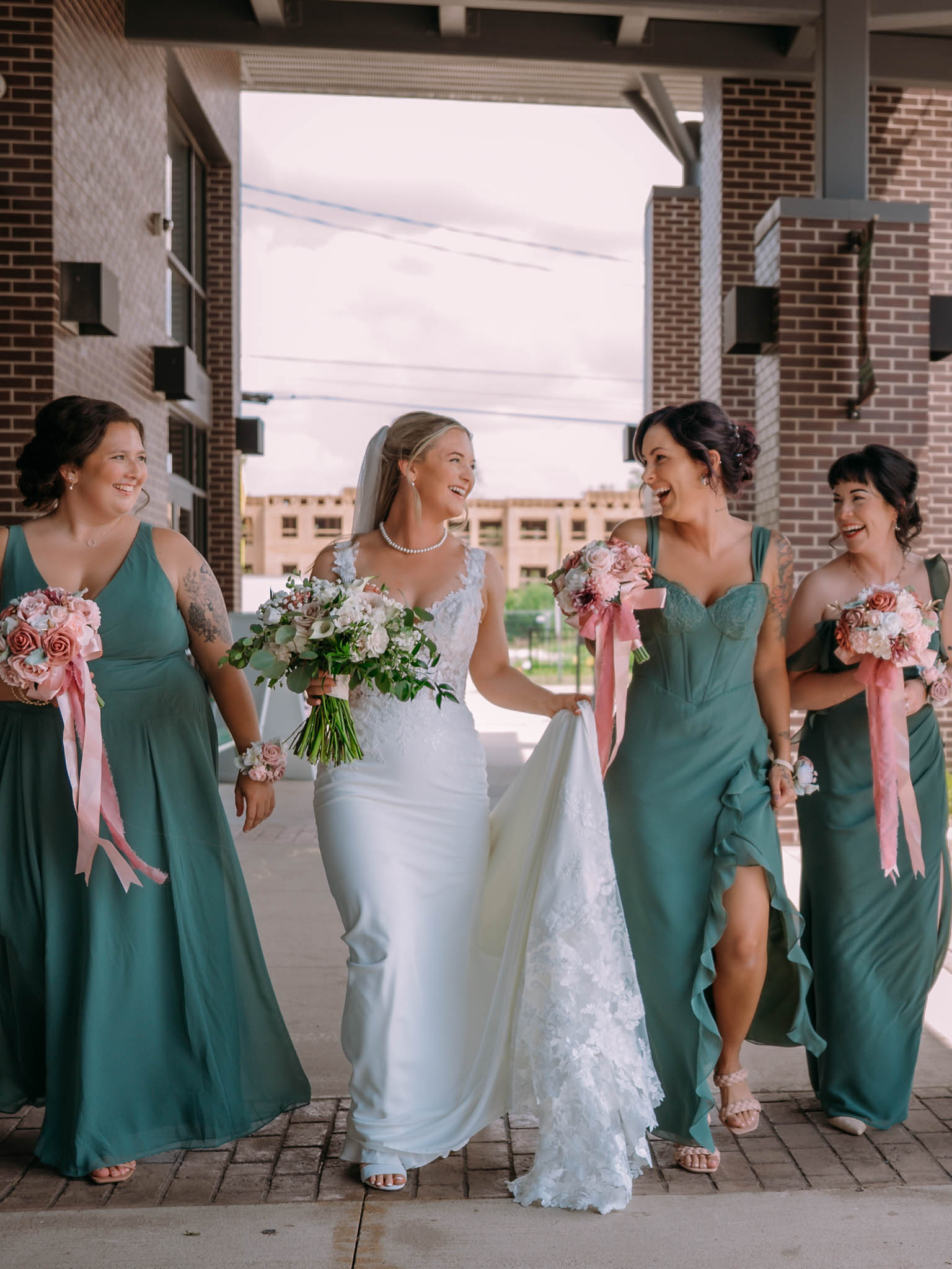 Bride walking with her bridesmaids who are in green dresses, outside of Terra Square in Hudsonville Michigan.